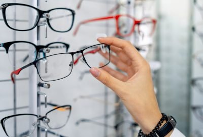 Row of glasses at an opticians. Eyeglasses shop. Stand with glasses in the store of optics. Woman's hand shows glasses. Presenting spectacles. Closeup